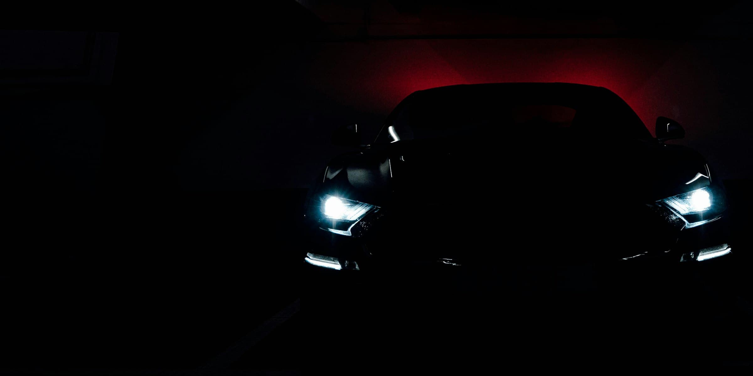 A dark performance car under red light in a workshop bay